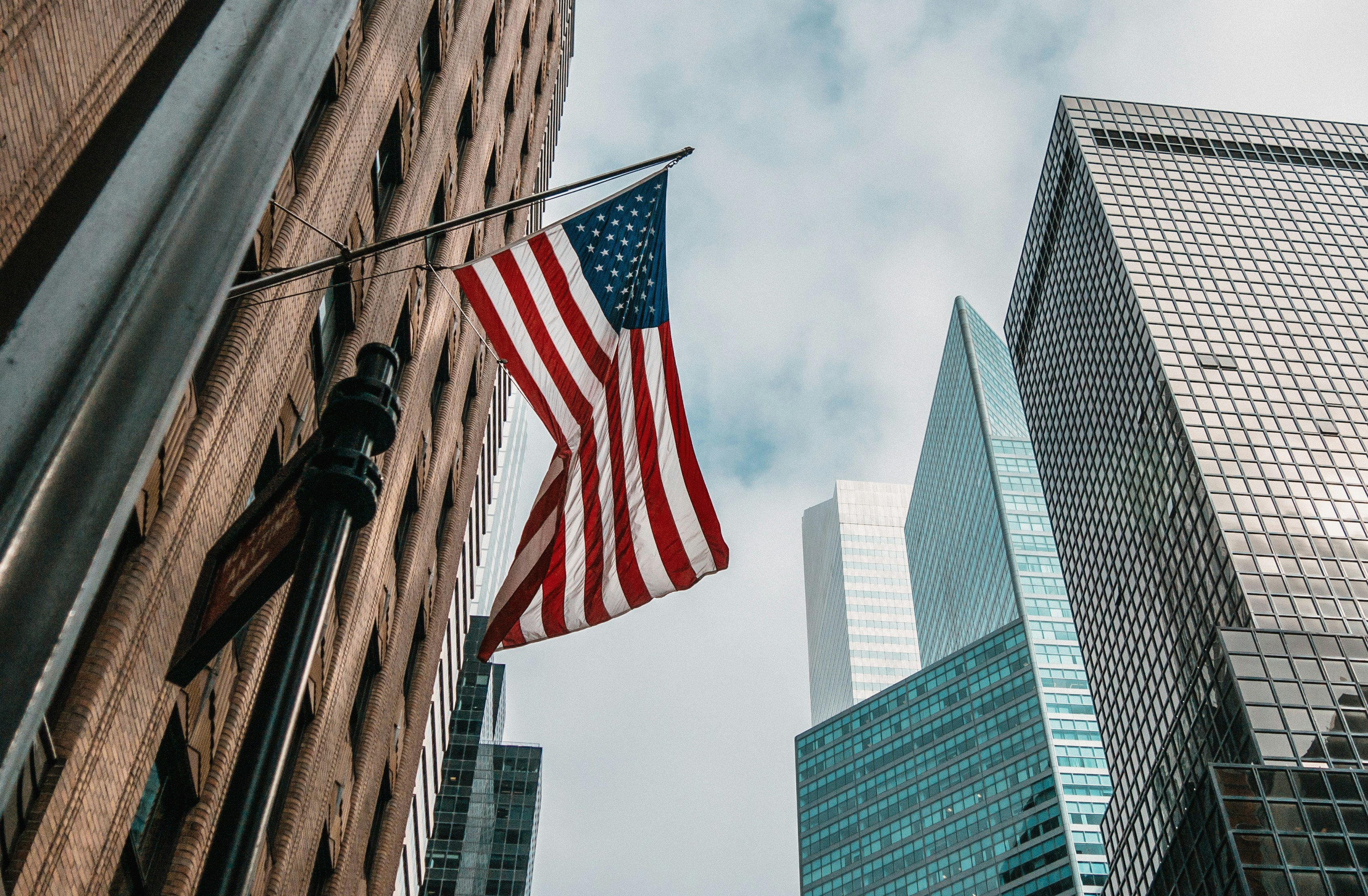 American flag surrounded by high rises in a city (Photo/Nik Shuliahin on Unsplash)