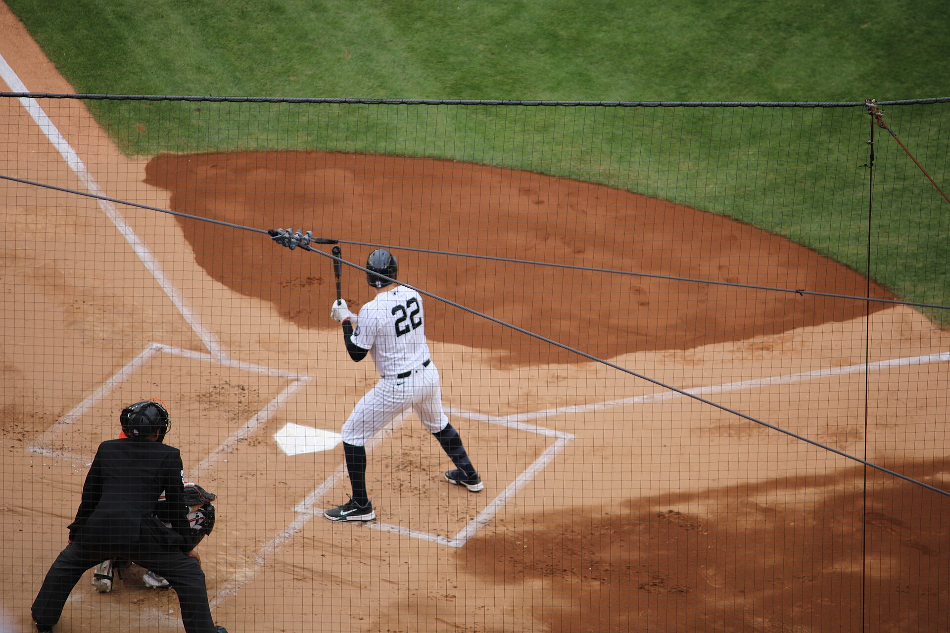 Yankees slugger Ben Rice, in home pinstripes and number 22, stands in the left-handed batter's box at Yankee Stadium with his bat raised, as the catcher and umpire crouch behind the plate.